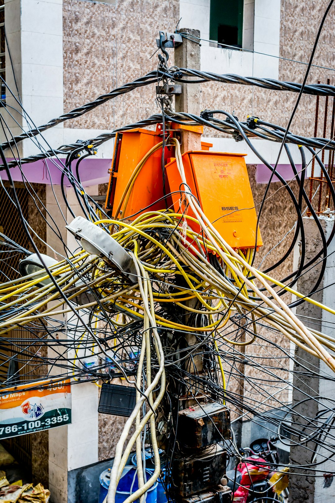 A utility pole covered in a chaotic tangle of black, yellow, and white cables wrapped around two orange electrical boxes marked "DANGER."
